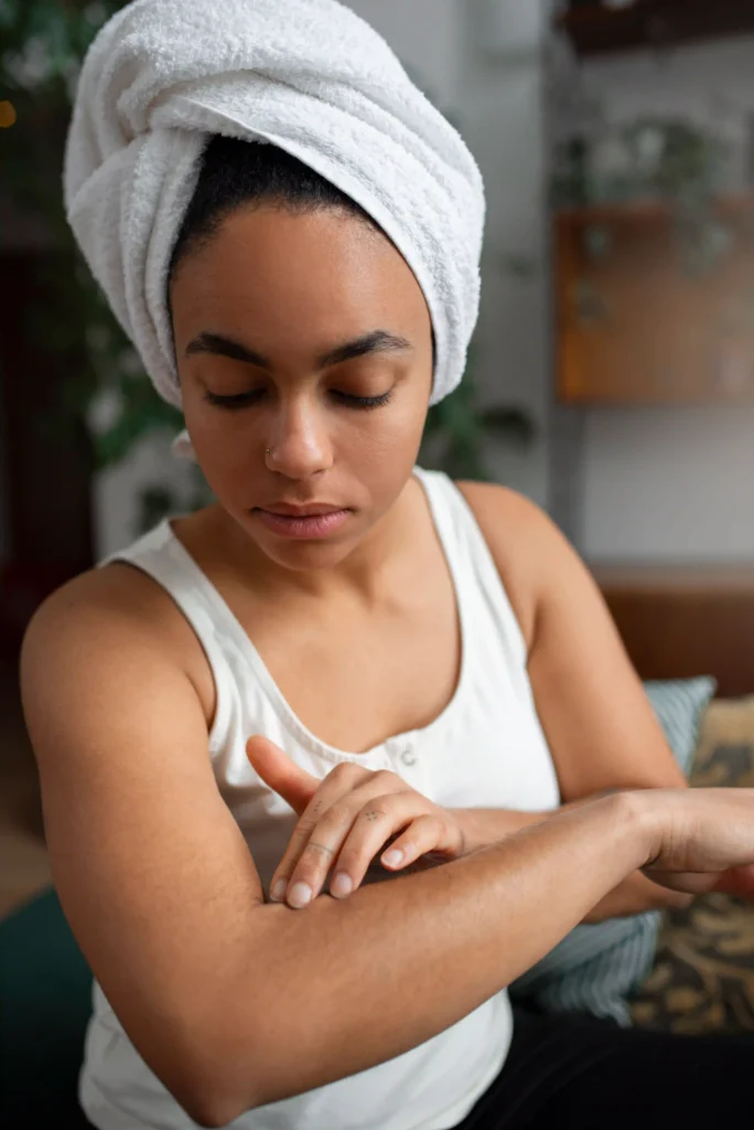 Woman applying moisturizer to her arm after shower to prevent dry skin.