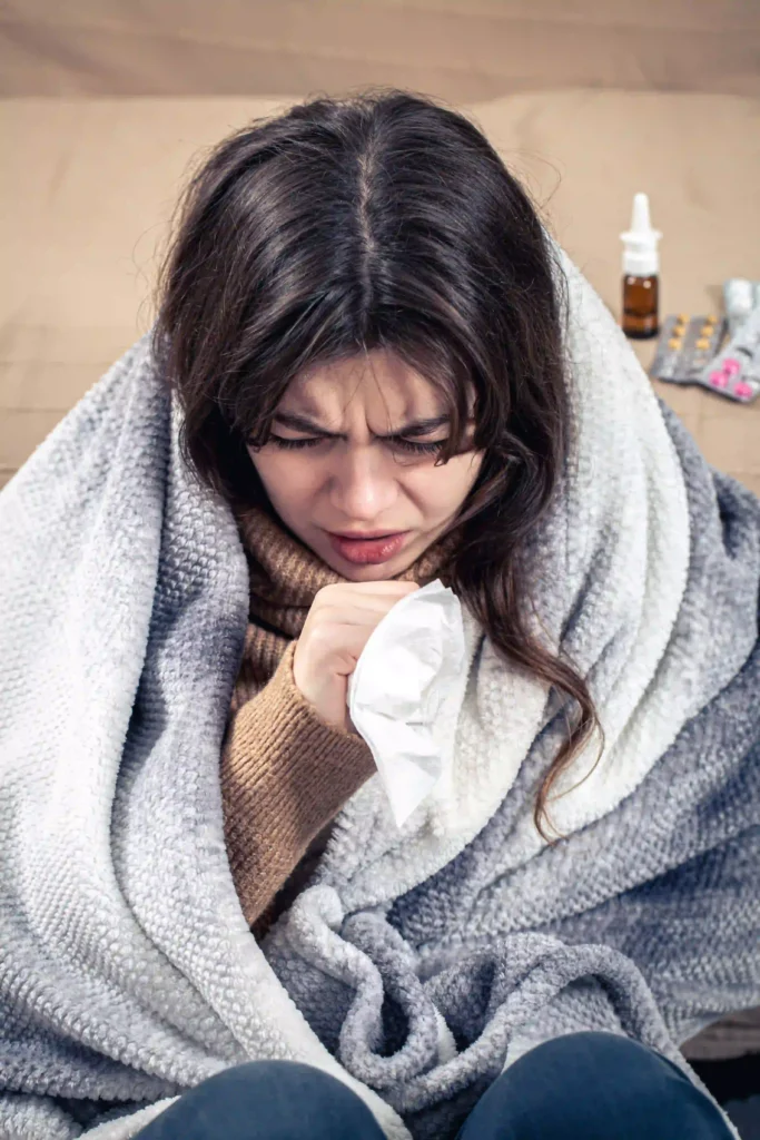 Sick woman with cough wrapped in blanket at home.